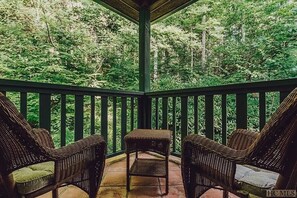 Un porche cubierto con muebles de mimbre y vistas a un bosque.