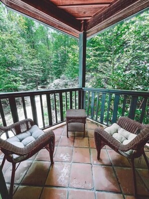 A covered outdoor area with wicker furniture and a view of a forest.
