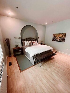 Une chambre à coucher comprenant un lit, un banc, une table de chevet, une lampe fixée au mur et un tableau.