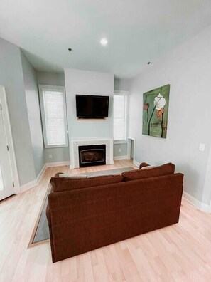 A living room with a flat-screen TV mounted above a fireplace, a brown sofa, and a painting on the wall.