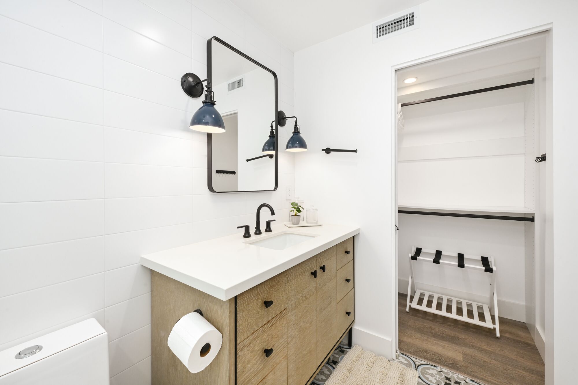 A modern bathroom with a white vanity, a mirror, two wall-mounted lights, a toilet, and a wooden cabinet.