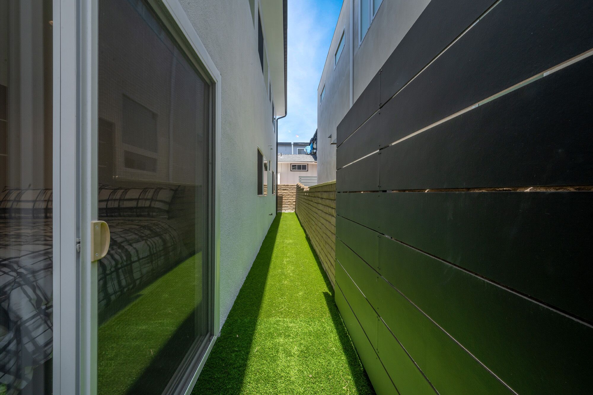 A narrow corridor with artificial grass, a sliding glass door, and a dark-colored wall.