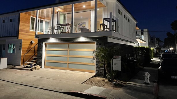 A modern two-story house with a large garage, a balcony with outdoor furniture, and a well-lit entrance. - 3 Bedroom Renovated Condo on Balboa Island (Newport Beach)