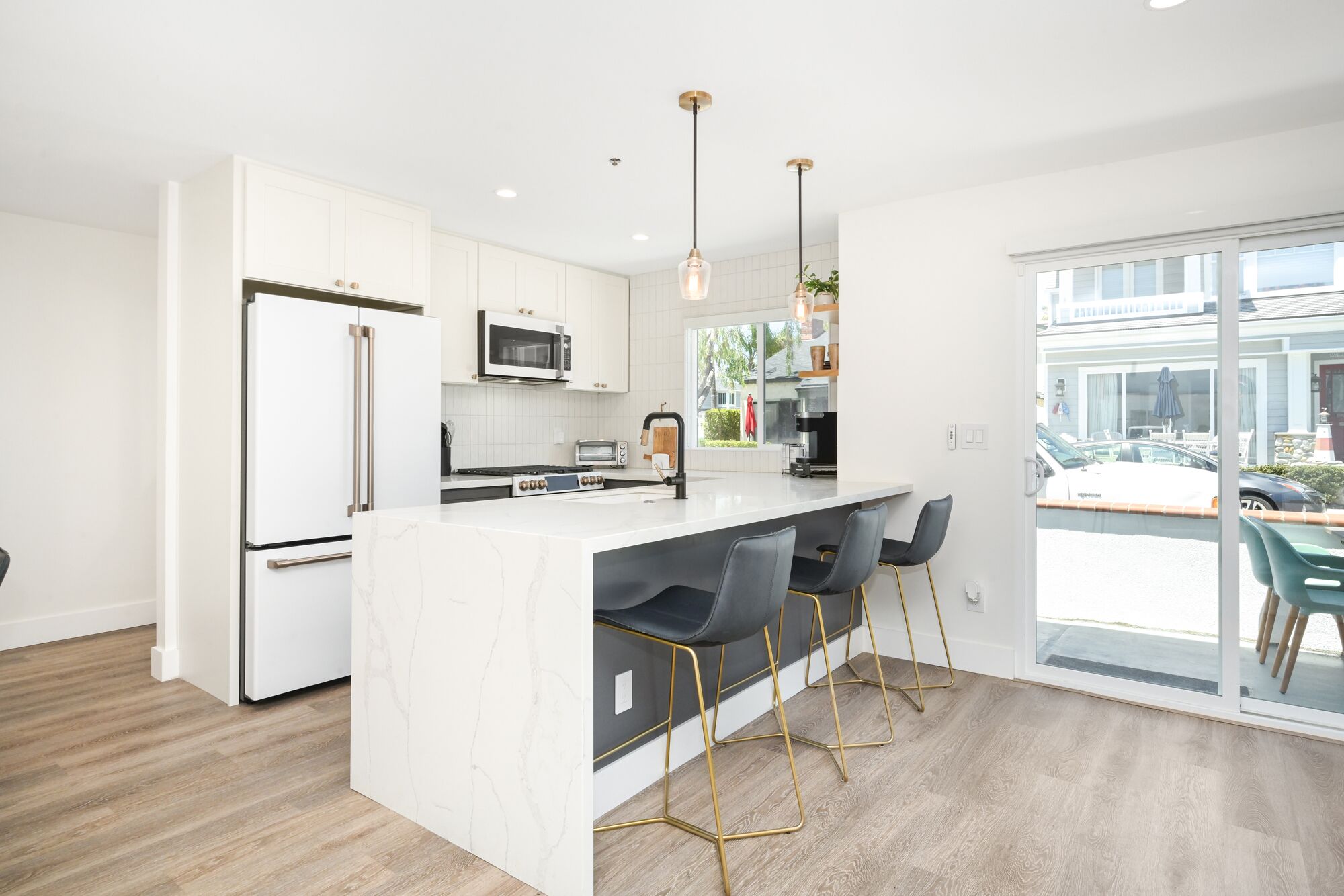 A modern kitchen with white cabinetry, a marble island, and a large window overlooking a parking area.