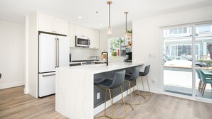 A modern kitchen with white cabinetry, a marble island, and a large window overlooking a parking area. - 3 Bedroom Renovated Condo on Balboa Island (Newport Beach)