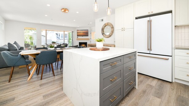 A modern kitchen with a marble island, grey cabinets, and stainless steel appliances.