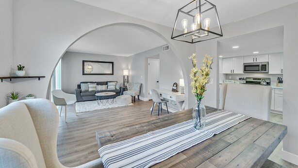 Ein modernes Wohnzimmer mit einem Holzesstisch, einer Sofagarnitur und einer Küche im Hintergrund.