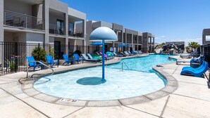 Une piscine avec des chaises et des parasols bleus, un toboggan aquatique et un bâtiment doté de balcons.