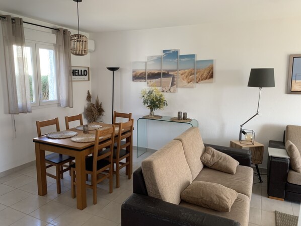 A modern living room with a wooden dining table, beige sofa, and a glass coffee table.