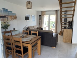 A modern living room with a dining area, featuring a wooden dining table, chairs, a sofa, and a staircase.
