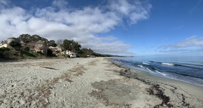 A beach with a sandy shore, a few scattered rocks, and a building with a round tower in the background.