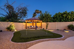 A gazebo with a patio, surrounded by a landscaped garden with a pool and a brick wall.