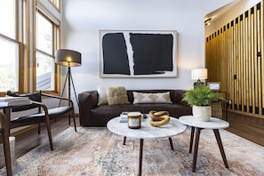 A modern living room with a brown leather sofa, a large abstract painting, a round coffee table with a plant, and a floor lamp.