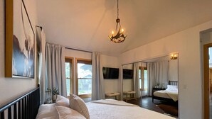 Une chambre à coucher avec un grand lit, un lustre, une télévision et un miroir.