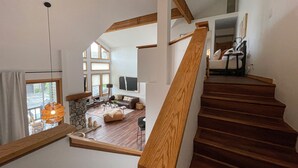 Un vaste espace de vie agrémenté d’un escalier en bois, d’une cheminée en pierre et d’une grande fenêtre laissant entrer la lumière naturelle.