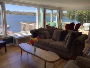 A living room with a large window overlooking a lake, a wooden coffee table, and a brown sofa with cushions.