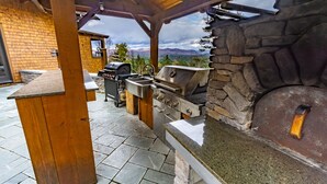 An outdoor kitchen area with a stone oven, a grill, and a wooden pergola. - Stunning Mountaintop Retreat with High End Amenities and Four Fireplaces (North Creek)