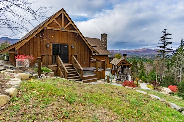 Une cabane en bois avec une cheminée en pierre, un porche à l’avant et un escalier menant à l’entrée.