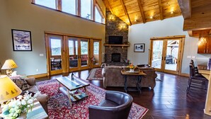 A spacious living room with a fireplace, large windows, and a high ceiling. - Stunning Mountaintop Retreat with High End Amenities and Four Fireplaces (North Creek)