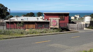 A coastal road with a red building, a signboard, and a view of the ocean. - Great location on a 9 hole, golf course, short walk to the ocean. (Shelter Cove)