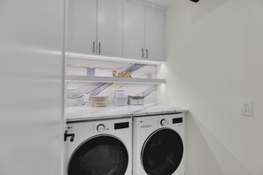 Un lavadero con dos lavadoras LG de carga frontal, armarios blancos y estantes con diseño de mármol.