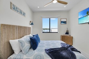 Un dormitorio con una cama grande, un ventilador de techo, una ventana con vista al mar y un cartel que dice 'SEAS THE DAY'.