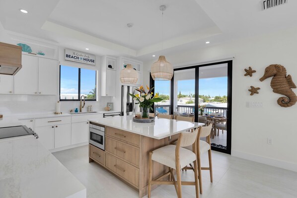 Una cocina moderna con una isla grande, armarios blancos y vistas al exterior.