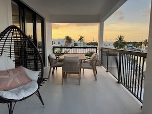 A balcony with a table and chairs, a wicker chair, and a view of a sunset over a marina. - Catch n' Relax Anglers Ultimate Waterfront Retreat, 50’ Dock, Pool Home Modern (Marathon)