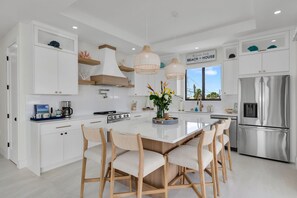 Una cocina moderna con armarios blancos, un refrigerador de acero inoxidable y una isla central con sillas.