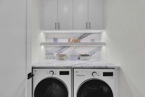 A laundry room with two front-loading washing machines, a marble countertop, and cabinets above. - Catch n' Relax Anglers Ultimate Waterfront Retreat, 50’ Dock, Pool Home Modern (Marathon)