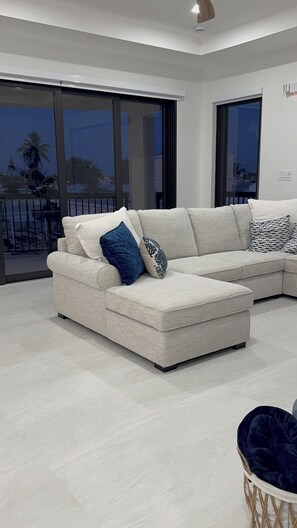 A modern living room with a sectional sofa, a large window, and a view of the outdoors. - Catch n' Relax Anglers Ultimate Waterfront Retreat with 50’ Dock Modern New Home (Marathon)