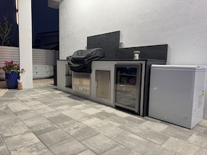 A modern outdoor kitchen area with a built-in refrigerator, a sink, and a cabinet. - Catch n' Relax Anglers Ultimate Waterfront Retreat, 50’ Dock, Pool Home Modern (Marathon)