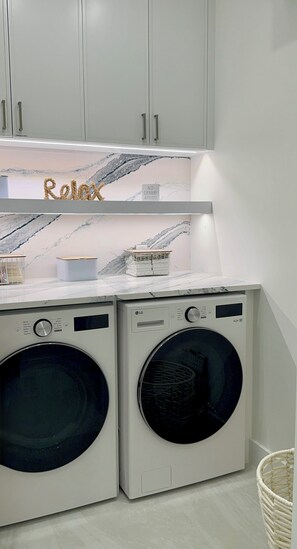 A laundry area with two front-loading washing machines, a drying rack, and a cabinet above. - Catch n' Relax Anglers Ultimate Waterfront Retreat with 50’ Dock Modern New Home (Marathon)