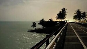 A coastal walkway with a railing, palm trees, and the sea in the background. - Catch n' Relax Anglers Ultimate Waterfront Retreat with 50’ Dock Modern New Home (Marathon)