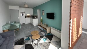 Una cocina moderna con armarios blancos, un comedor con una mesa y sillas verdes, y una sala de estar con un sofá y una mesita de centro.