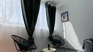 Una habitación moderna con dos sillas negras de estructura metálica, una mesita redonda con una planta y un sofá gris.