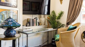 A living room with a television, a glass-top coffee table, a wicker chair, and a potted plant. - Mayfair Centre 3-Bed 6-Guest Art Nouveau Flat in 1729 Private House (London)