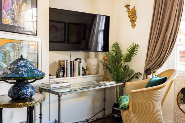 Una sala de estar con televisor, una mesa de centro de vidrio, una silla de mimbre y una planta en maceta.