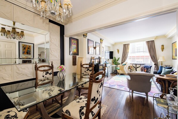 A spacious living room with a glass dining table, elegant chairs, and a comfortable sofa.