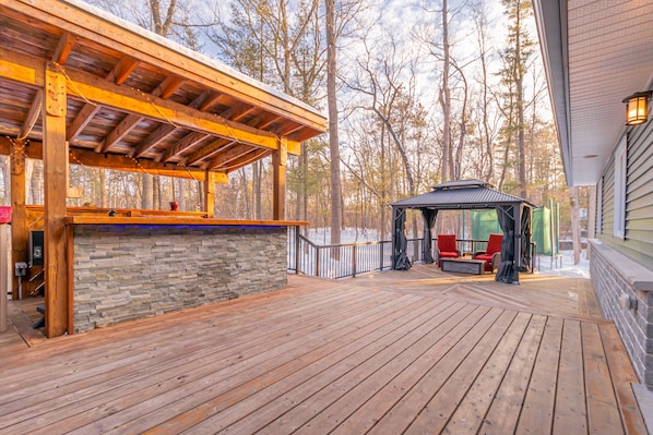 A wooden deck with a stone wall, a covered seating area, and a gazebo.