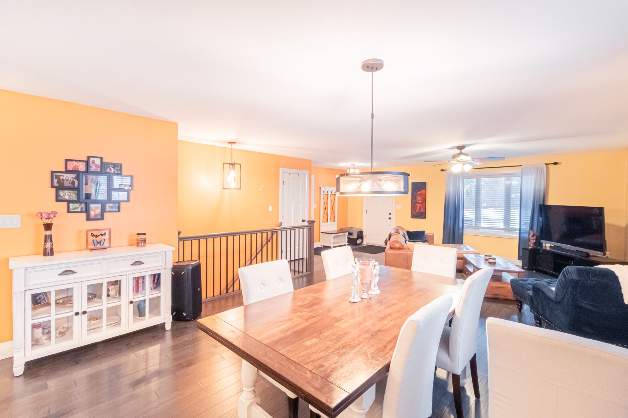 A dining area with a wooden table, white chairs, a white cabinet, and a television in the background.