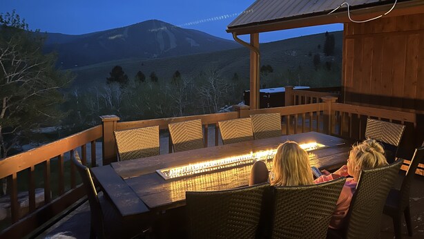 Una terraza de madera con una mesa y sillas, con vistas a un paisaje montañoso.