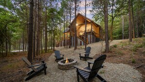 En stuga med en eldstad av sten och fyra Adirondack-stolar, belägen i en skogsmiljö.