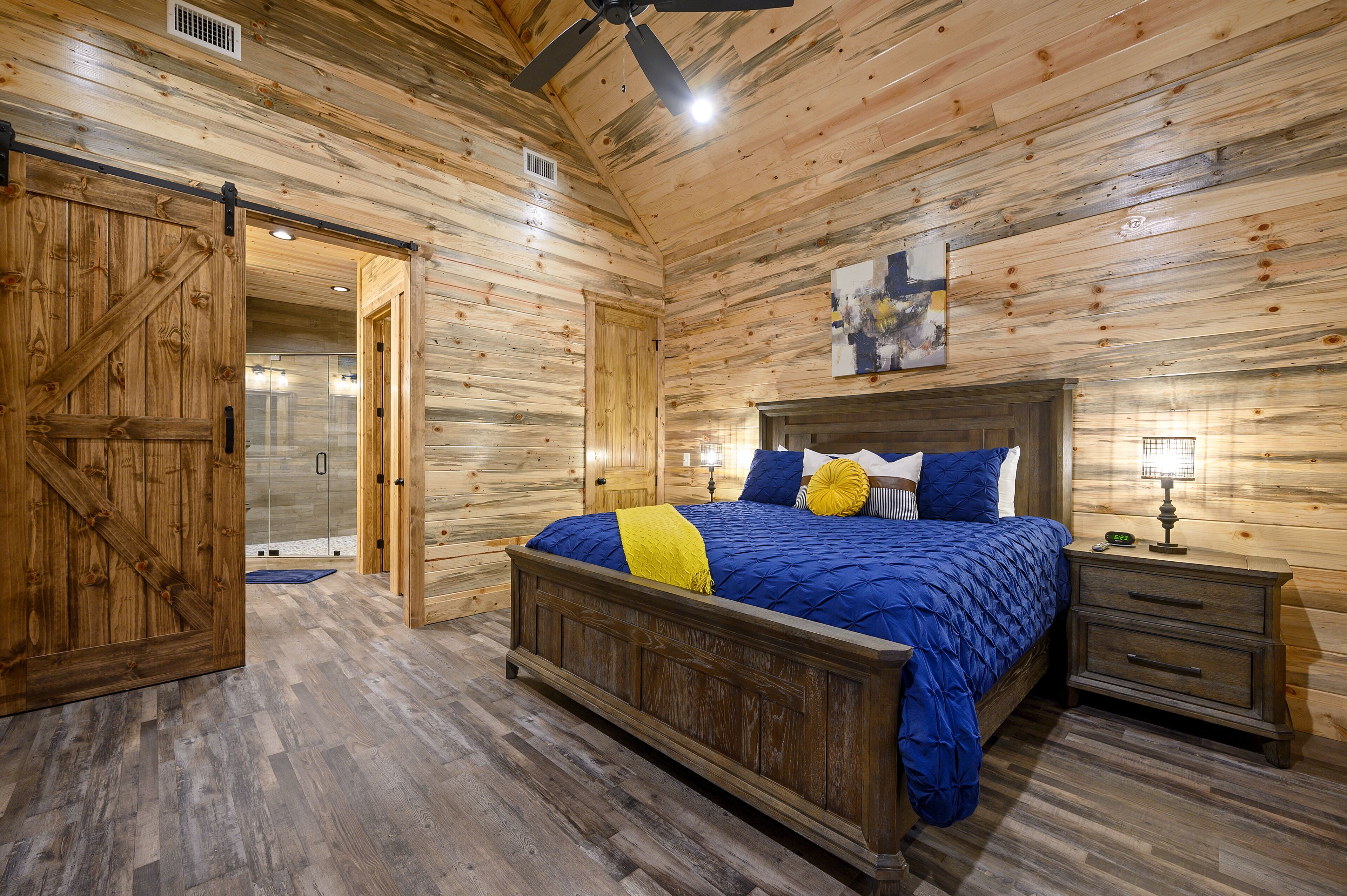 Une chambre à coucher aux murs lambrissés, avec un lit, une table de chevet et une porte donnant sur une salle de bain.