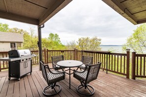 A covered deck with a grill, four wicker chairs, and a table.