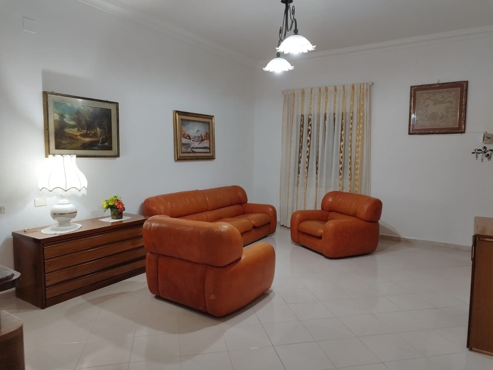 A living room with a sofa, a lamp, and two paintings on the wall.