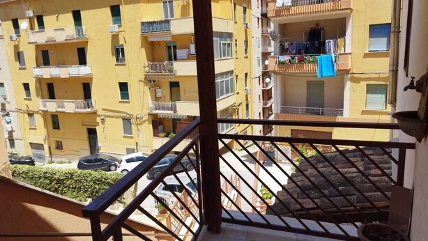 Ein Balkon mit Blick auf gelbe Wohngebäude, einem Blumentopf und einem darunter geparkten Auto.