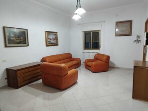 Un soggiorno con un divano, una poltrona, un mobile in legno e due quadri appesi al muro.