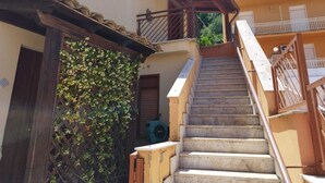 Eine Treppe führt zu einem Balkon mit Holzgeländer, einer Tür mit Holzrahmen und einer mit Kletterpflanzen bewachsenen Wand.