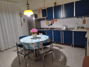 A kitchen with blue cabinets, a white tiled backsplash, a stainless steel sink, and a dining table with chairs.